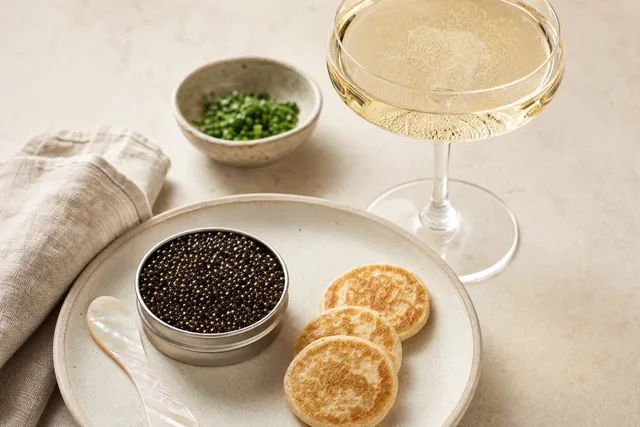 A glass of champagne beside an open tin of caviar.